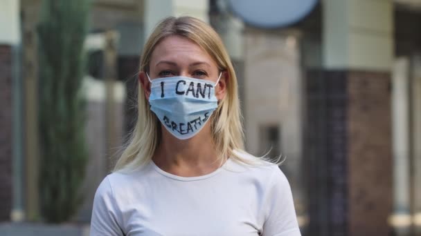 Dicht dramatisch buitenportret van een jonge blanke vrouw in een medisch masker met de inscriptie die ik niet kan ademen. BLM-beweging, zwarte levens materie, steun voor massale protesten tegen racisme. Langzame beweging. — Stockvideo