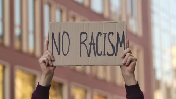 남성 손은 도시의 배경에 NO RACISM 이라는 슬로건이 붙은 포스터를 들고 있다. 시위 포스터는 야외에서 닫습니다. 거리 시위. 닫아. 느린 동작. — 비디오
