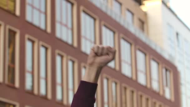 Opgeheven mannelijke hand met gebalde vuist voor protest tegen de achtergrond van een hoogbouw. Protest tegen racisme en politiegeweld. Sluit maar af. Langzame beweging. — Stockvideo