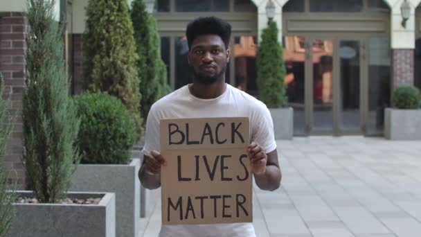 Uomo afroamericano con in mano un poster con l'iscrizione Black lives Matter. Studente nero in una maglietta bianca si trova su una strada della città. Manifestazione di strada. Al rallentatore. Da vicino.. — Video Stock