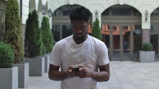Portrait de jeune homme afro-américain est message texte puis pointe vers le smartphone de la caméra avec écran vert et clé chromatique. Il touche l'écran et montre son pouce. Au ralenti. Gros plan. — Video