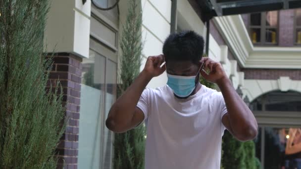 Portret młodego Afroamerykanina patrzącego w kamerę i zakładającego ochronną maskę medyczną. Koncepcja ochrony zdrowia wirusa korony. Zwolnij trochę. Zamknij się.. — Wideo stockowe