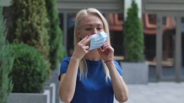 Çekici bir genç kadının portresi kameraya bakıyor ve koruyucu bir tıbbi maske takıyor. Corona virüsü sağlık koruma konsepti. Ağır çekim. Kapat..