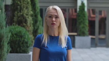 Çekici bir genç kadının portresi kameraya bakıyor ve biriyle konuşuyor. Caddenin arka planında mavi bluzlu bir sarışın var. Ağır çekim. Kapat..