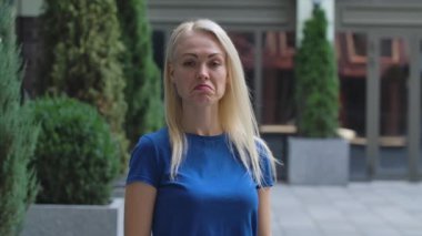 Çekici bir genç kadının portresi kameraya bakıyor ve dikkatle dinliyor ve başını sallıyor. Caddenin arka planında mavi bluzlu bir sarışın var. Ağır çekim. Kapat..