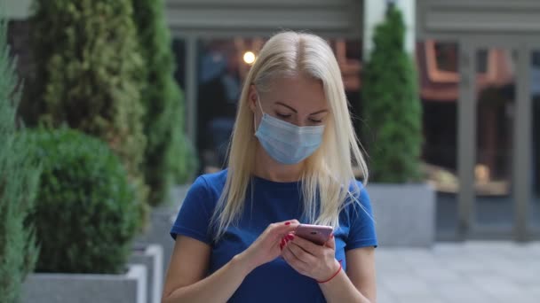 Retrato de una encantadora joven con una máscara médica protectora está enviando mensajes de texto y hablando en su teléfono inteligente. Concepto de protección de salud del virus Corona. En cámara lenta. De cerca.. — Vídeos de Stock