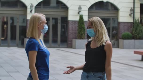 Dos mujeres jóvenes con máscaras médicas protectoras se saludan en la calle con codos y se comunican. Concepto de protección de salud del virus Corona. En cámara lenta. De cerca.. — Vídeos de Stock