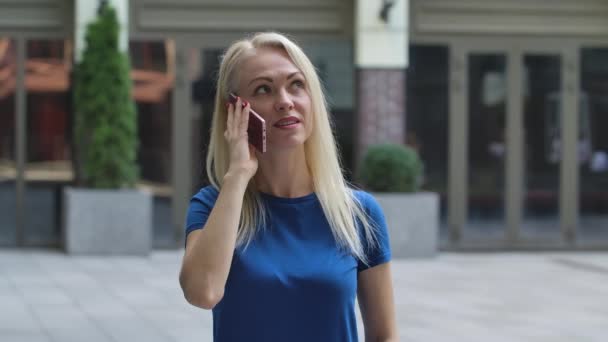 Porträtt av en charmig ung kvinna som pratar på sin smartphone. Blond i en blå blus utomhus på bakgrunden av gatan. Sakta i backarna. Närbild. — Stockvideo