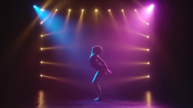 Siyahlar içinde profesyonel bir balerin. Dinamik spot ışıkları altında zarif bir şekilde bale yapıyor ve sahnede sigara içiyor. Güzel, ince bir siluetin silueti.