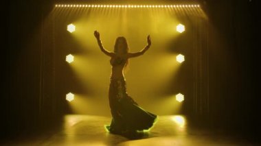 Güzel bir dansçı doğu dansının klasik hareketlerini sergiliyor. Siluet yarı çıplaklık. Duman ve neon ışıkla karanlık bir stüdyoda çekildi. Yavaş çekim.