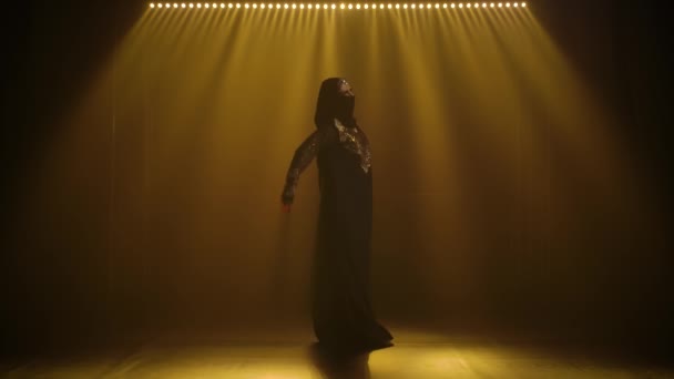 Silhuett mage dansare kvinna dansar i en svart orientalisk klänning och hijab. Skjuten i en mörk studio med rök och neonljus. Långsamma rörelser. — Stockvideo