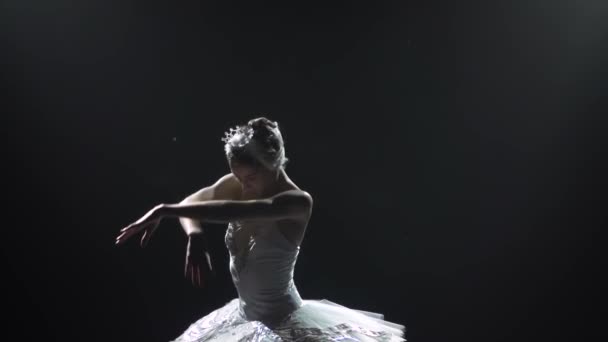 年轻美丽优雅的芭蕾舞演员穿着白色燕尾服伴奏的古典芭蕾舞。苗条身材的轮廓.在摄影棚的聚光灯背景下在黑暗中拍摄。慢动作. — 图库视频影像