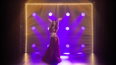 Geleneksel oryantal dansçı kız duman ve mavi neon ışıklı arka planda dans ediyor. Yavaş çekim.