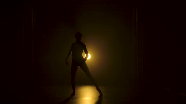 Silhueta uma bailarina flexível fina em bodysuit preto dança graciosa na escuridão sob um teatro holofotes amarelos de estúdio. — Vídeo de Stock