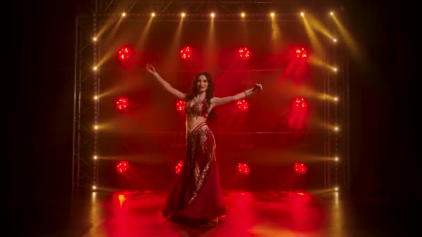 Kobieta w egzotycznym stroju wykonuje taniec brzucha porusza pół nagie ciało. Kręcony w ciemnym studiu z dymem i czerwonym neonem. Zwolniony ruch. — Wideo stockowe