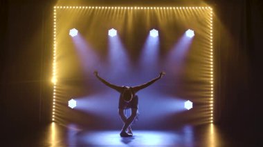 Profesyonel balerin sahne ışıkları altında bale yapıyor ve sahnede sigara içiyor. Güzel, ince bir siluetin silueti.