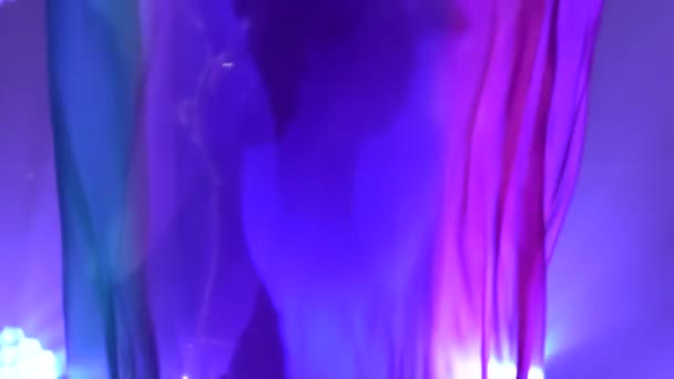 Female belly dancer in a white oriental costume dancing with silk cloth. Shot in a dark studio with smoke and blue neon lighting. Silhouettes of a slender flexible body. Close up. Slow motion. — Stock Video