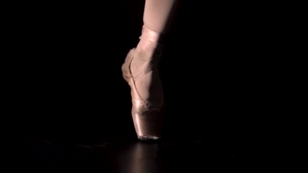 Graceful legs of a ballerina in white pointe shoes. Ballerina shows classic ballet pas. Shot in a darkness on spotlights background of studio. Close up. — Stock Video