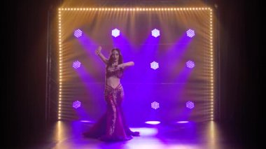 Geleneksel oryantal dansçı kız duman ve mavi neon ışıklı arka planda dans ediyor. Yavaş çekim.