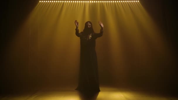 Silhouette exotische Bauchtänzerin, die in einem schwarzen orientalischen Kleid und Hijab tanzt. Gedreht in einem dunklen Studio mit Rauch und Neonlicht. — Stockvideo