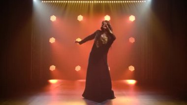 Siyahi bir oryantal elbiseyle dans eden egzotik dansçı kadın. Karanlık bir stüdyoda duman ve neon ışıkla çekildi..