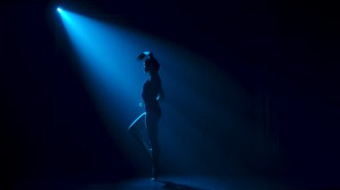 Siluet. Siyah elbiseli, esnek bir balerin. Stüdyonun mavi sahne ışıkları altında karanlıkta zarif bir şekilde dans ediyor..