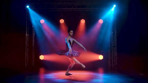 Anmutige Ballerina im schicken Bild eines schwarzen Schwans. Tanz der Elemente des klassischen Balletts. Gedreht in einem dunklen Studio mit Rauch und magischer Neonbeleuchtung. Zeitlupe. — Stockvideo