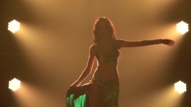 Güzel dansçı kadın karanlık bir stüdyoda dumanlı ve neon ışıklı zarif oryantal dans ediyor. İnce, esnek bir vücudun siluetleri. Kapatın. Yavaş çekim.