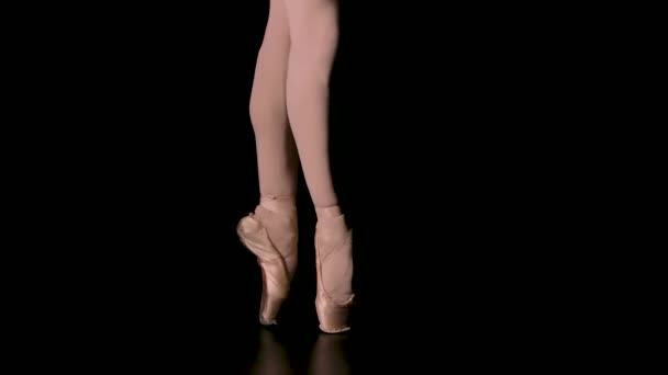 Χαριτωμένα πόδια μιας μπαλαρίνας με άσπρα πουέντ παπούτσια. Μπαλαρίνα δείχνει κλασικό pas μπαλέτου. Πυροβολήθηκε σε ένα σκοτάδι σε προβολείς φόντο στούντιο. Κλείσε. Αργή κίνηση. — Αρχείο Βίντεο