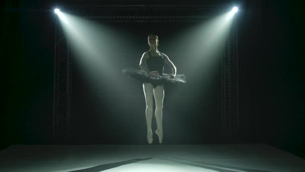 Silhouette egy fiatal balerina fekete tütüben és pointe balett cipőben. Klasszikus balett elemek kecses tánca. Sötétben forgatták egy színházi reflektorfényben a stúdió fekete hátterében.. — Stock videók