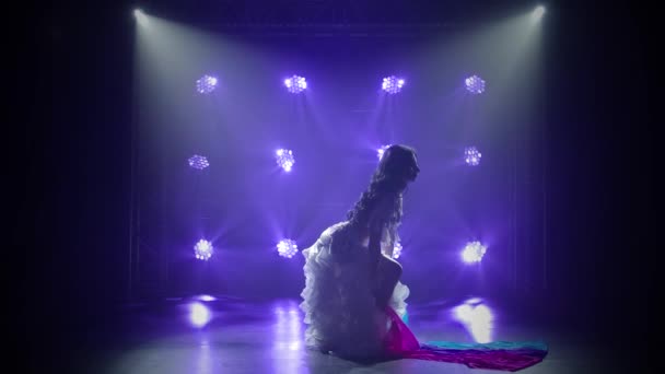 Bailarina del vientre femenina en un traje oriental blanco bailando con tela de seda. Grabado en un estudio oscuro con humo e iluminación de neón azul. Siluetas de un cuerpo delgado y flexible. Movimiento lento. — Vídeo de stock