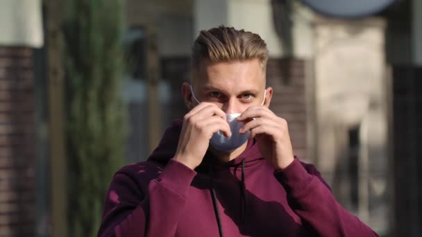 Portrait of a young man looking at the camera and putting on a medical mask to protect his face from the nCov-19 coronavirus. COVID-19 prevention measures. Slow motion. Face close up . — Stock Video