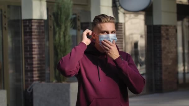 Portrait de jeune homme regardant la caméra et mettant un masque médical sur le visage pour se protéger contre le coronavirus nCov-19. COVID-19 mesures préventives. Au ralenti. Gros plan. — Video