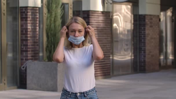 Portrait of pretty young woman looking into the camera and putting on medical mask on face for protection against coronavirus nCov-19. COVID-19 preventive measures. Slow motion. Close up. — Stock Video