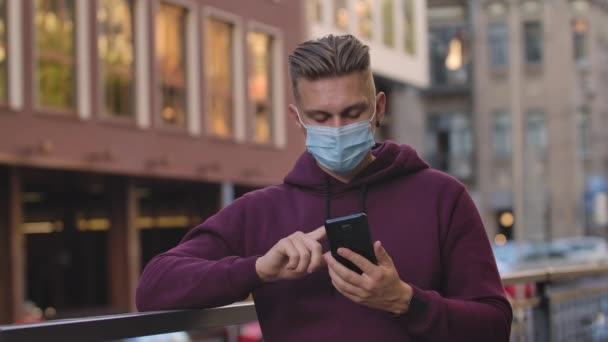 Portrét mladého muže v lékařské masce je textová zpráva a pak ukazuje na fotoaparát smartphone se zelenou obrazovkou a chroma klíčem. COVID-19 preventivní opatření. Zpomal. Zavřít.