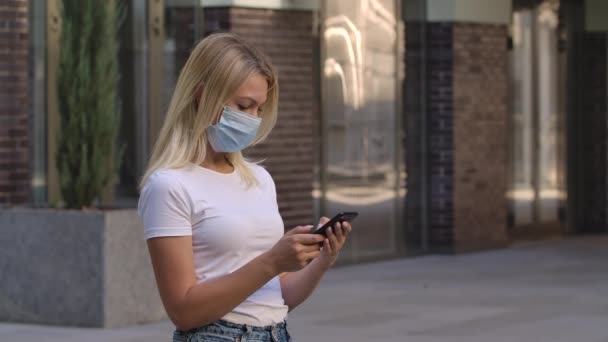 Egy csinos fiatal nő arcképe védő orvosi maszkban sms-t küld az okostelefonjára, vagy közösségi oldalakon kommunikál. COVID-19 megelőző intézkedések. Oldalnézetből. Lassú mozgás. Közelről.. — Stock videók