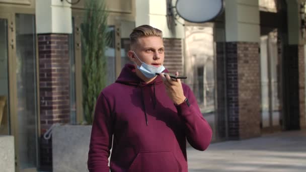 Porträt eines jungen Mannes mit gesenkter medizinischer Maske spricht auf ihrem Smartphone über das Lautsprechertelefon. COVID-19 Präventivmaßnahmen. Zeitlupe. Nahaufnahme. — Stockvideo