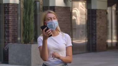 Koruyucu tıbbi maske takan güzel genç bir kadının portresi akıllı telefonuyla konuşuyor. COVID-19 önleyici önlemler. Yan görüş. Ağır çekim. Kapat..