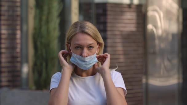 Güzel bir genç kadının portresi kameraya bakıyor ve Coronavirus nCov-19 'a karşı korunmak için yüzüne tıbbi maske takıyor. COVID-19 önleyici önlemler. Ağır çekim. Kapat.. — Stok video