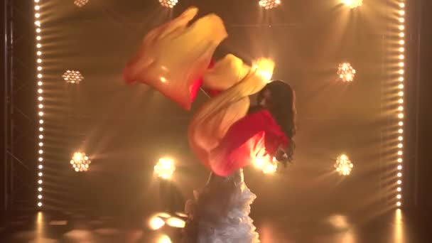 Femme danseuse du ventre dans un costume oriental blanc dansant tissus ventilateur de soie. Tourné dans un studio sombre avec de la fumée et un éclairage au néon. Ferme là. Mouvement lent. — Video