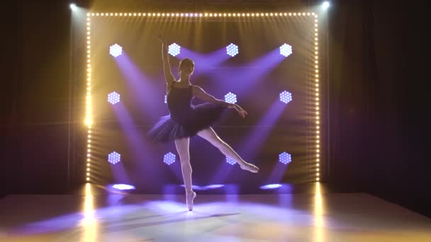 Giovane ballerina flessibile in tutù nero e scarpe da balletto a punta. Danza graziosa di elementi balletto classico. Girato in un buio su sfondo riflettori. Silhouette di una bella figura sottile. — Video Stock