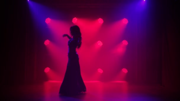 Silhouette Mädchen in einem orientalischen Kostüm führt klassischen Bauchtanz auf. Gedreht in einem dunklen Studio mit Rauch und roter Neonbeleuchtung.