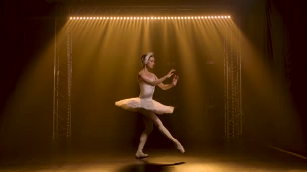 Klassisk balettkoreografi fulländad av ung vacker graciös ballerina i vit tutu. Vit svan del i föreställningen av kvinnlig konstnär. Skjuten i ett mörker på gul spotlights bakgrund. — Stockvideo