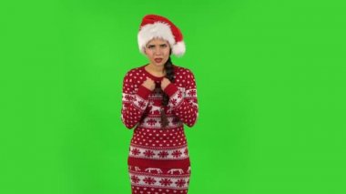 Noel Baba şapkalı tatlı kız kendini masum gösteriyor, parmağını şakağına doğru kıvırıyor. Yeşil Ekran