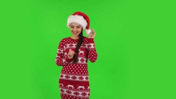 Милая девочка в шляпе Санта Клауса кокетливо улыбается, глядя в камеру. Зеленый экран — стоковое видео