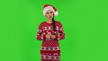 Noel Baba şapkalı tatlı kız dikkatle dinliyor ve kafasını izleyiciyi işaret ediyor. Yeşil Ekran