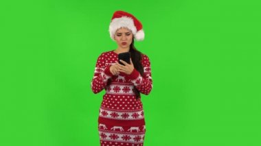 Noel Baba şapkalı tatlı kız öfkeyle telefonuna mesaj atıyor. Yeşil Ekran