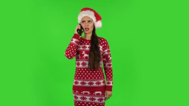 Милая девочка в шляпе Санта Клауса гневно разговаривает за мобильный телефон. Зеленый экран — стоковое видео