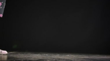 Siyah arka planda, karanlık bir stüdyoda beyaz mokasen giyen bir kadının bacakları görünüyor. Ayakkabılar ve bacaklar kapalı. Yavaş çekim.