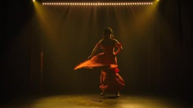 Karanlık bir stüdyoda ateşli bir şekilde flamenko yapan orta yaşlı bir kadının silueti. Yanan esmer, uzun kırmızı elbiseli, dumanlı arka planda, sarı ışıklı. Yavaş çekim.